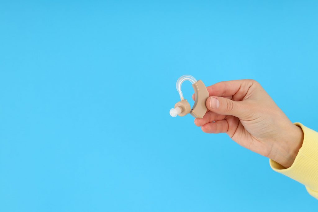 Female hand holds hearing aid on blue background